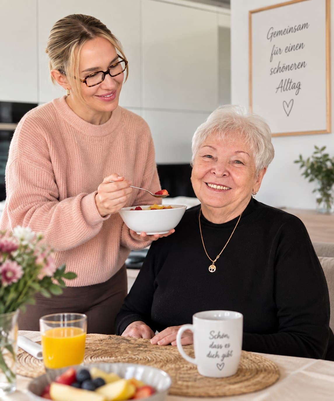 Betreuungskraft reicht einer lachenden Seniorin am Frühstückstisch frisches Obst
